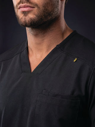 Close-up of a man wearing a dark navy V-neck scrub top with a chest pocket and a small yellow logo on the shoulder.