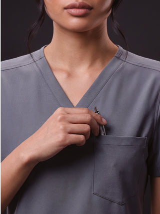 Kyur women's slate gray V-neck scrub top, close-up of chest pocket holding a pen